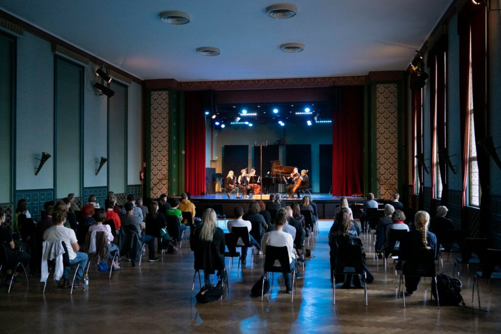 Uusinta Ensemble esiintyy yleisölle. Katsomossa on isot turvavälit tuolien välissä.