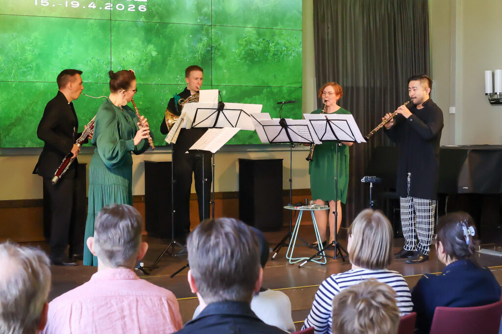 Yhtye soittaa puhallinmusiikkia lavalla, yleisö istuu edessä katsomassa.