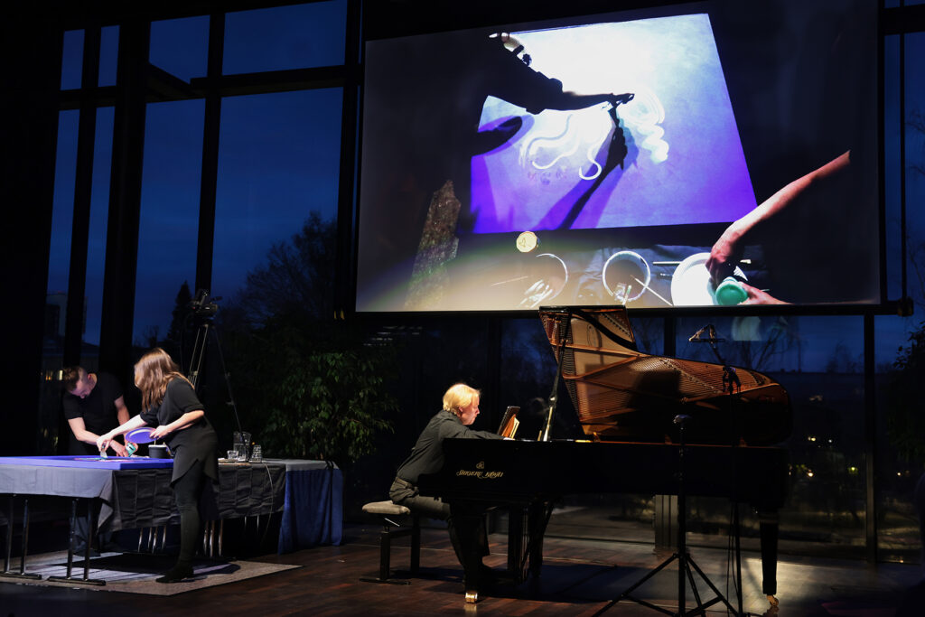 Yllä heijastus livemaalauksesta, alla Ville Hautakangas soittaa pianoa.
